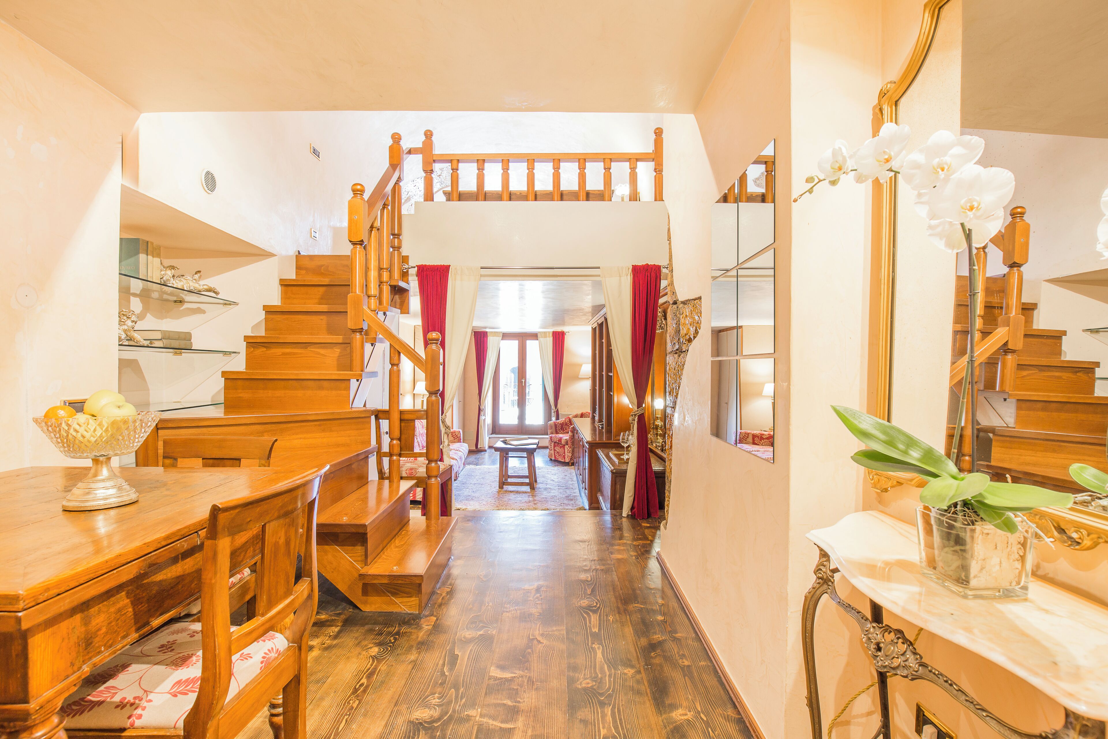 A wooden staircase leading to a second floor, a dining area with wooden furniture, and a marble table with a plant.