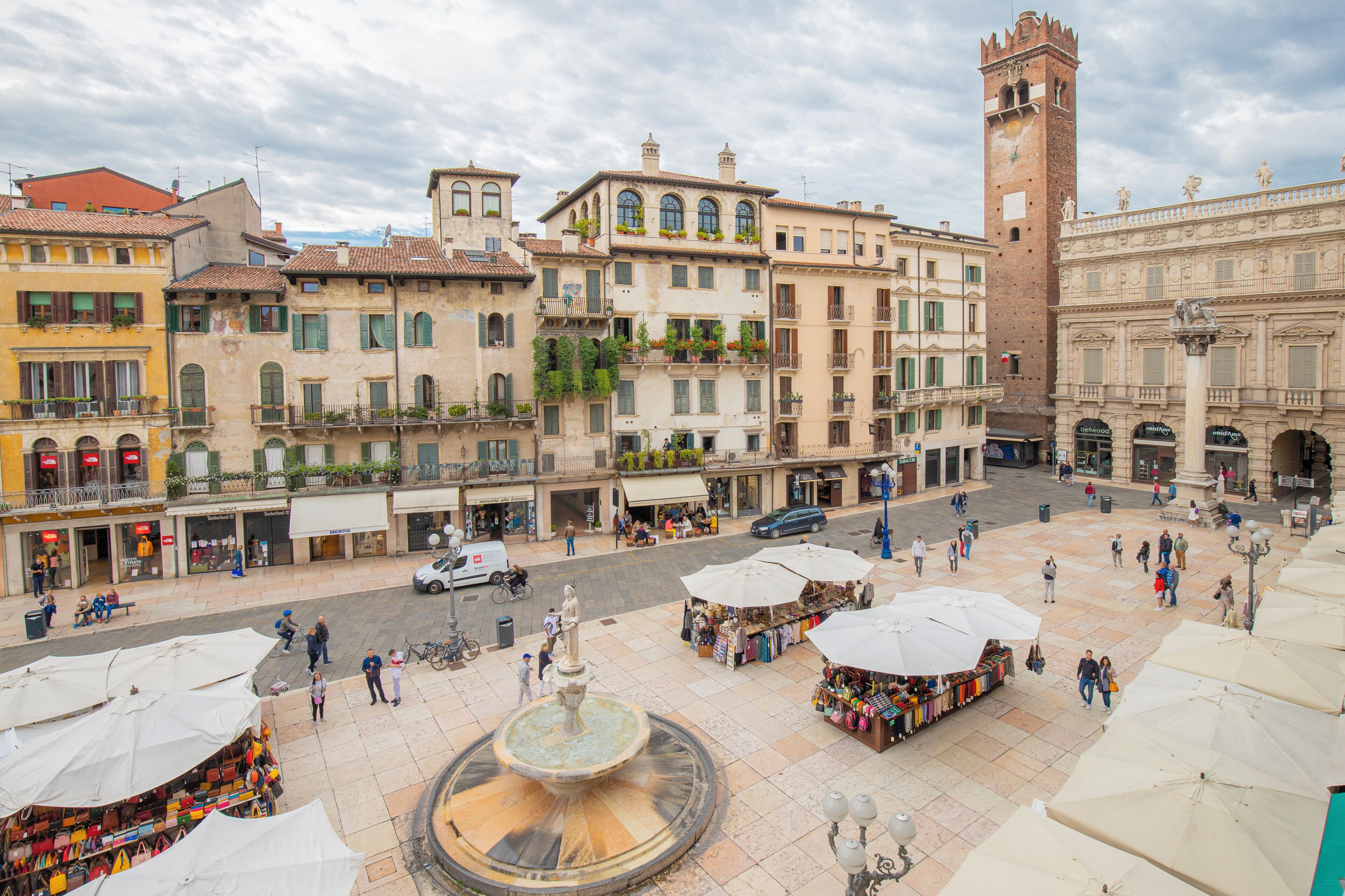 A square with a fountain, surrounded by historic buildings and outdoor market stalls.