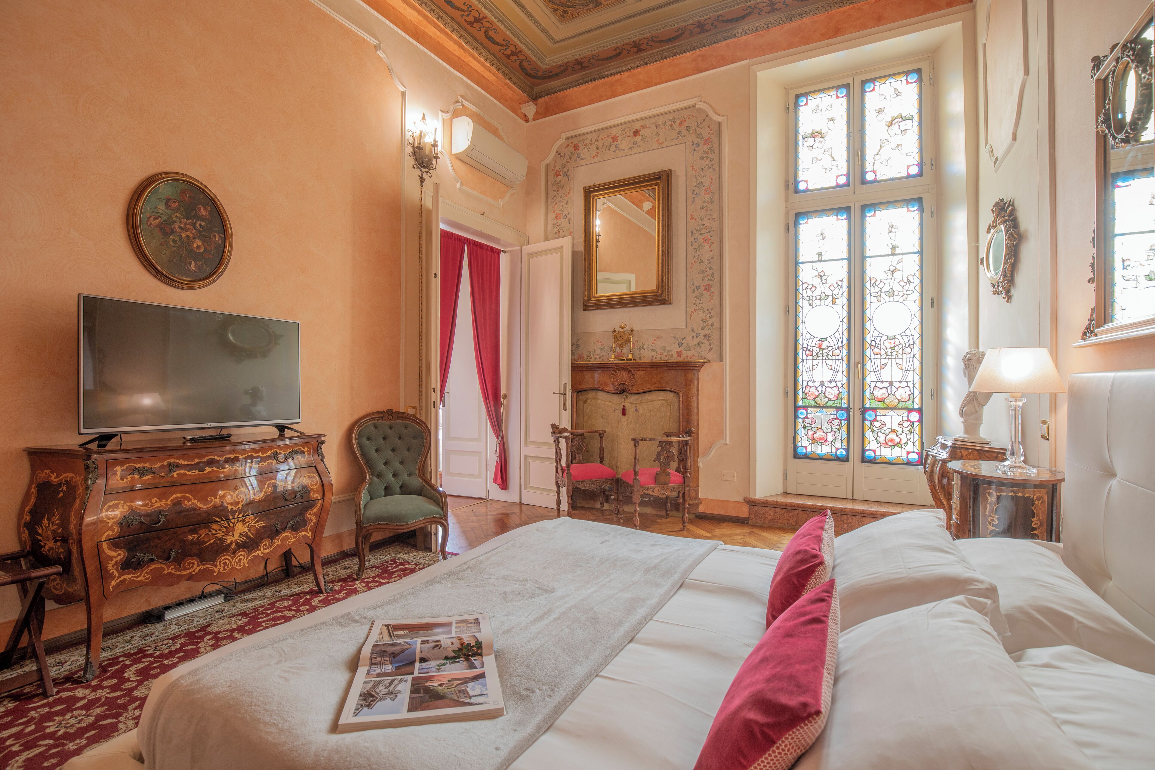 Habitación de hotel con una cama grande, televisión, chimenea y vistas al exterior a través de ventanales con vidrieras.