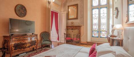 Habitación de hotel con una cama grande, televisión, chimenea y vistas al exterior a través de ventanales con vidrieras.