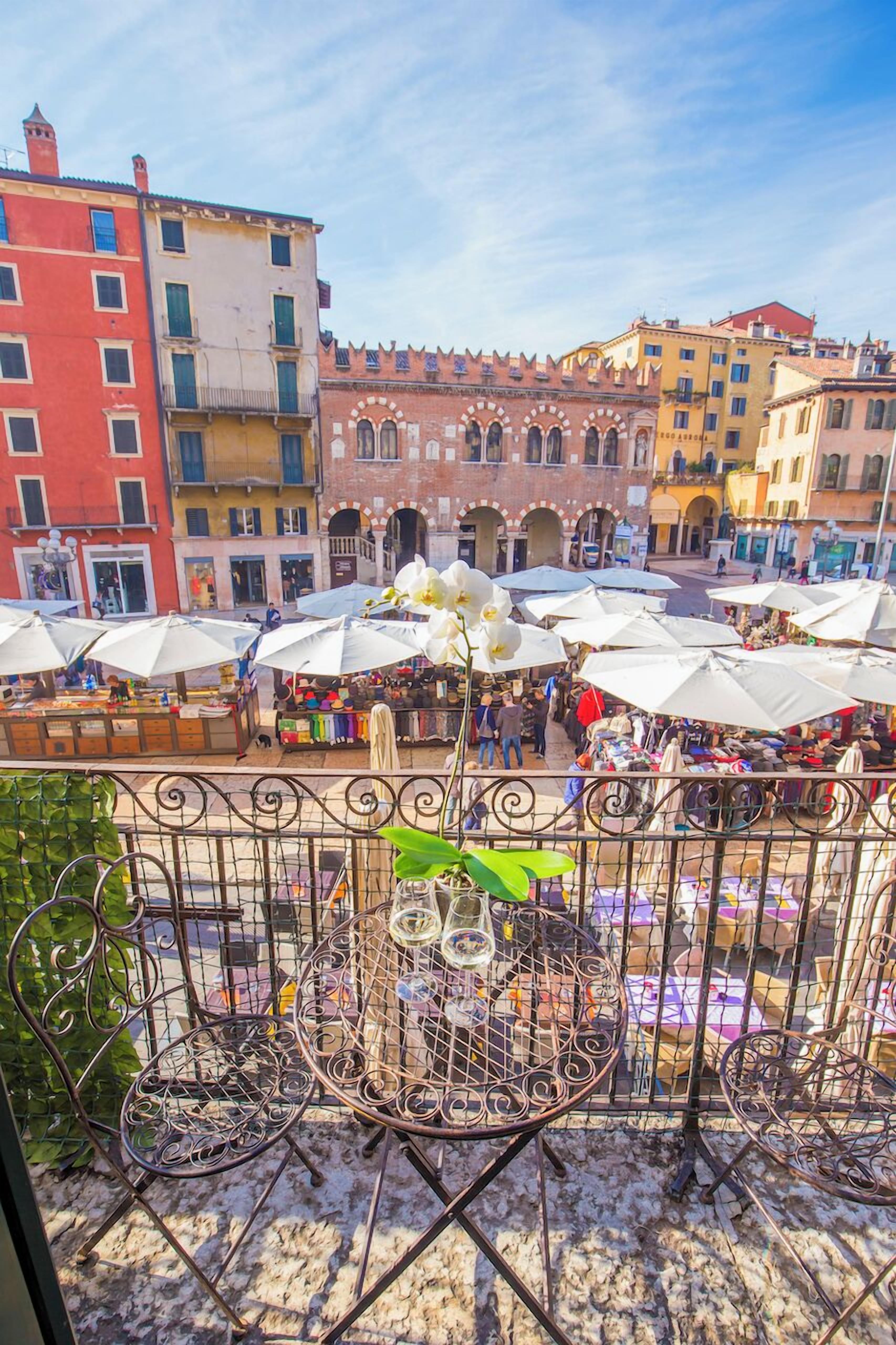 A balcony with metal chairs and a table, overlooking a bustling outdoor market with umbrellas and people.