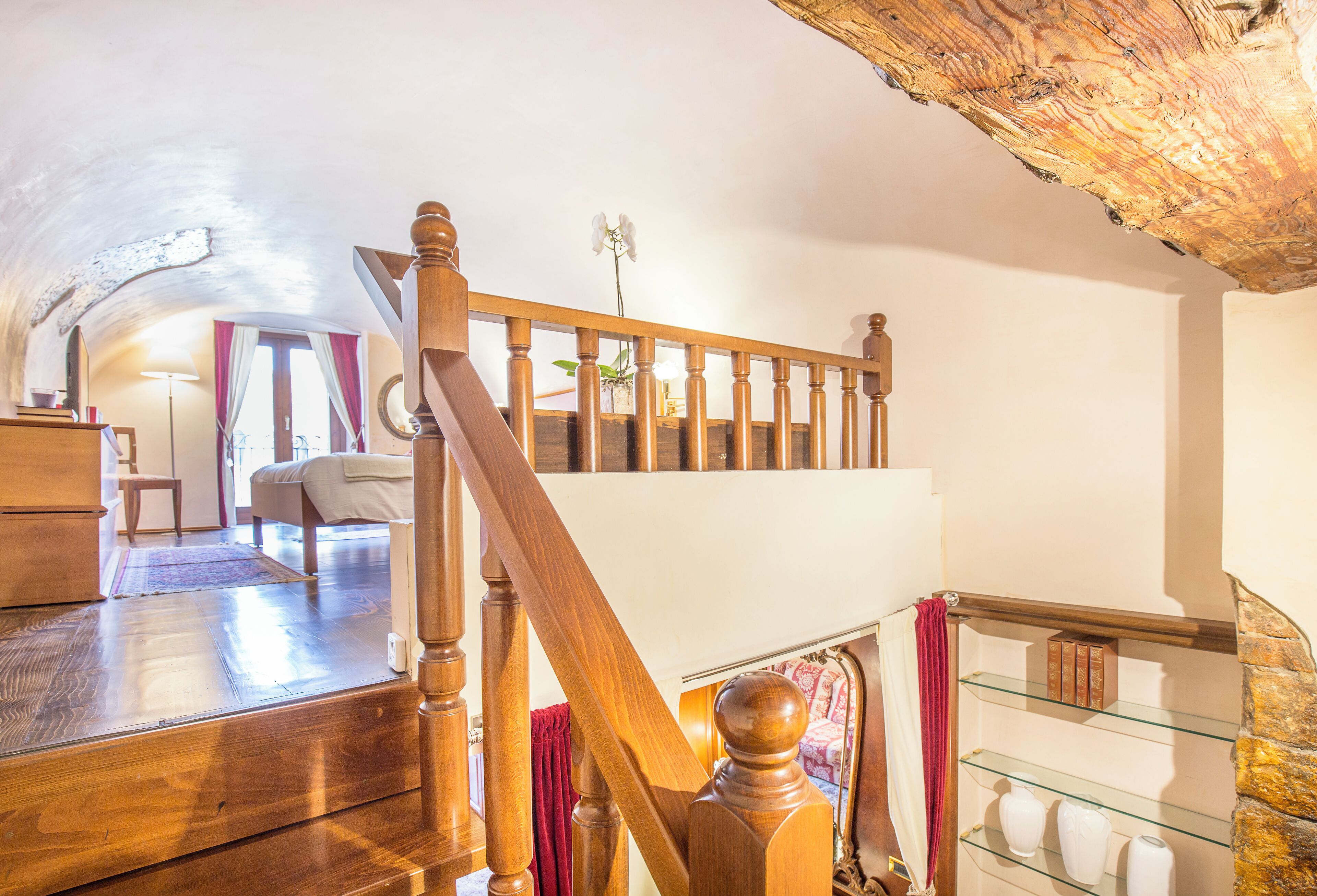 A wooden staircase with a glass railing leading to a second-floor bedroom with a bed and a window.