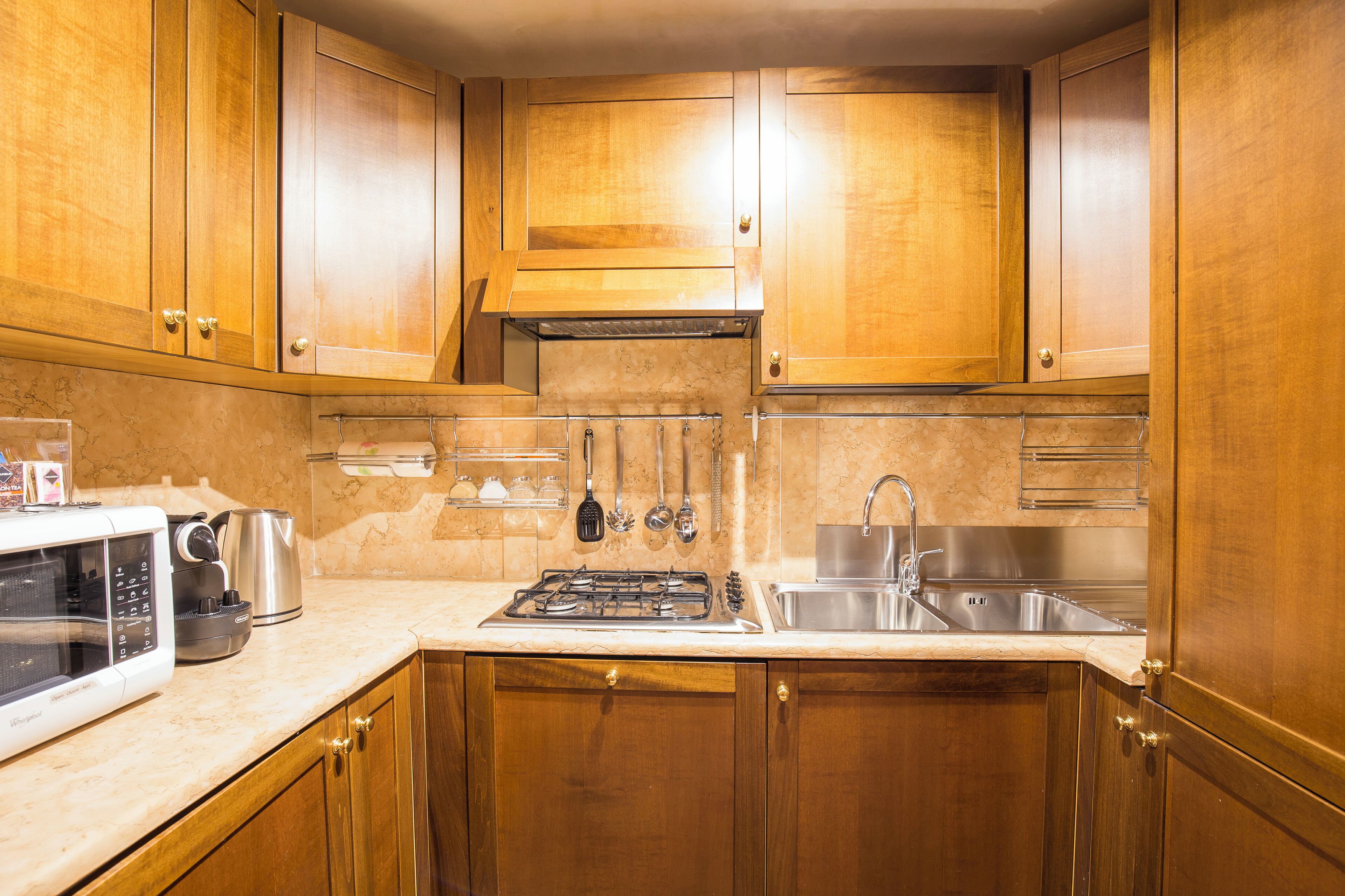 A kitchen with wooden cabinets, a gas stove, a microwave, a kettle, and a sink.