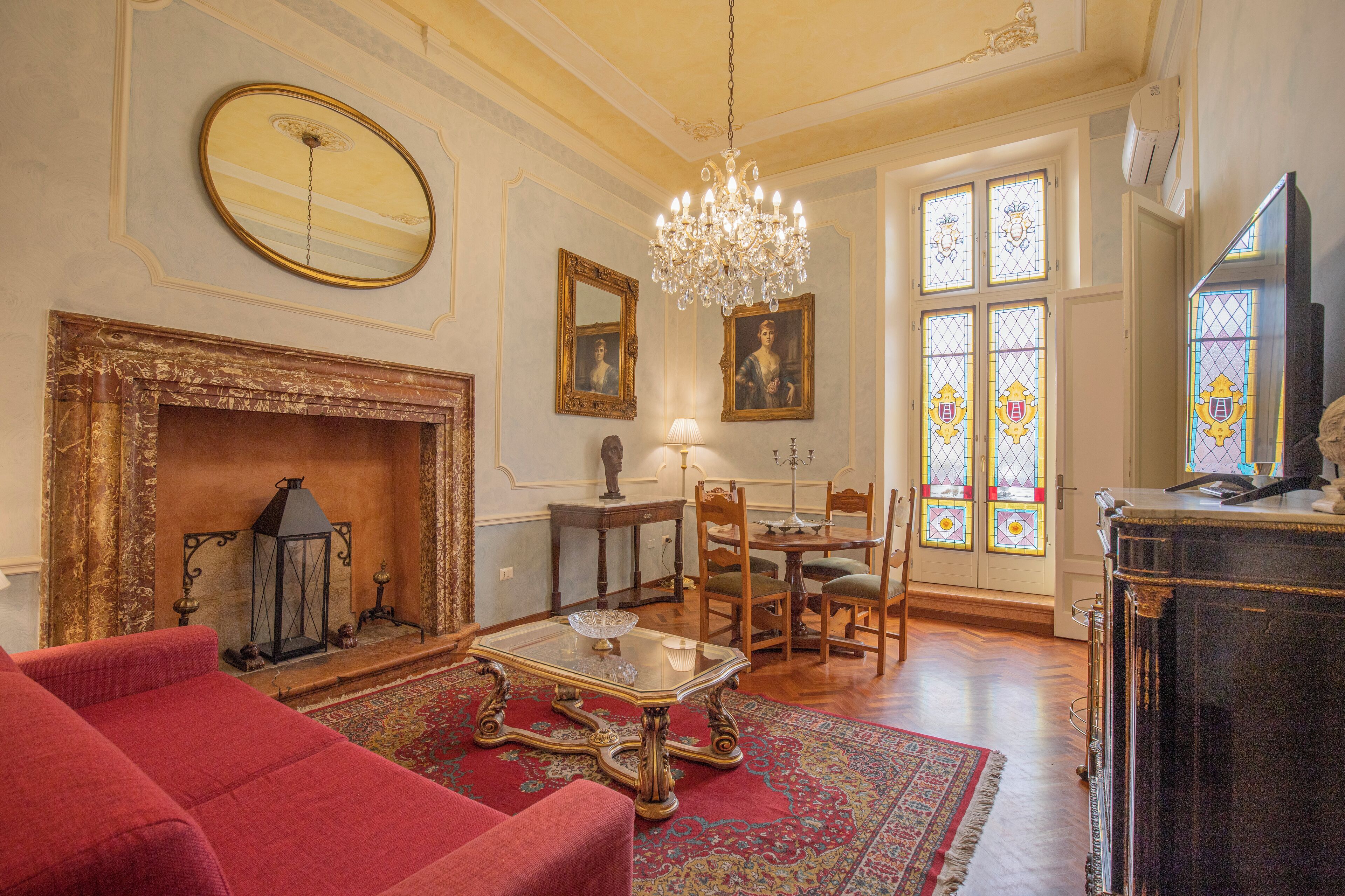 A room with a fireplace, a chandelier, a dining table with chairs, and a television.