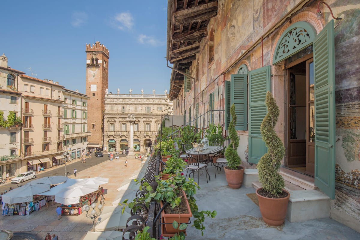 A courtyard with a fountain, potted plants, outdoor seating, and a historic building with a tower.