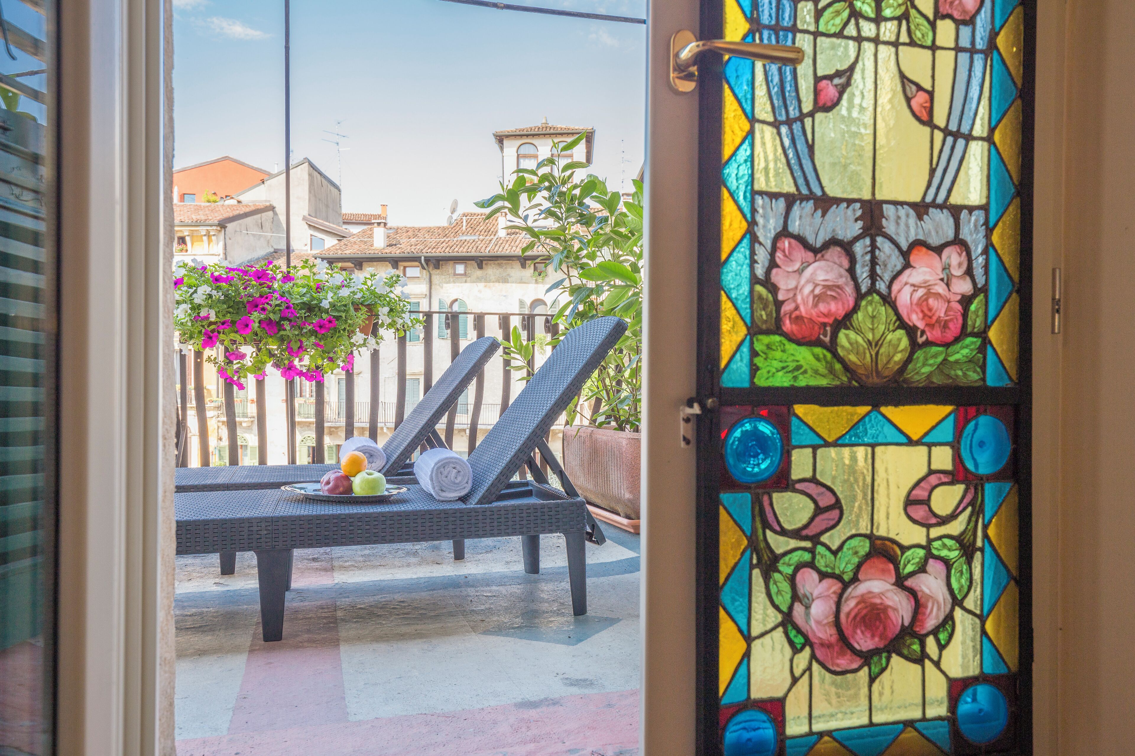 A balcony with two lounge chairs, a table with fruits, and a potted plant with pink flowers.
