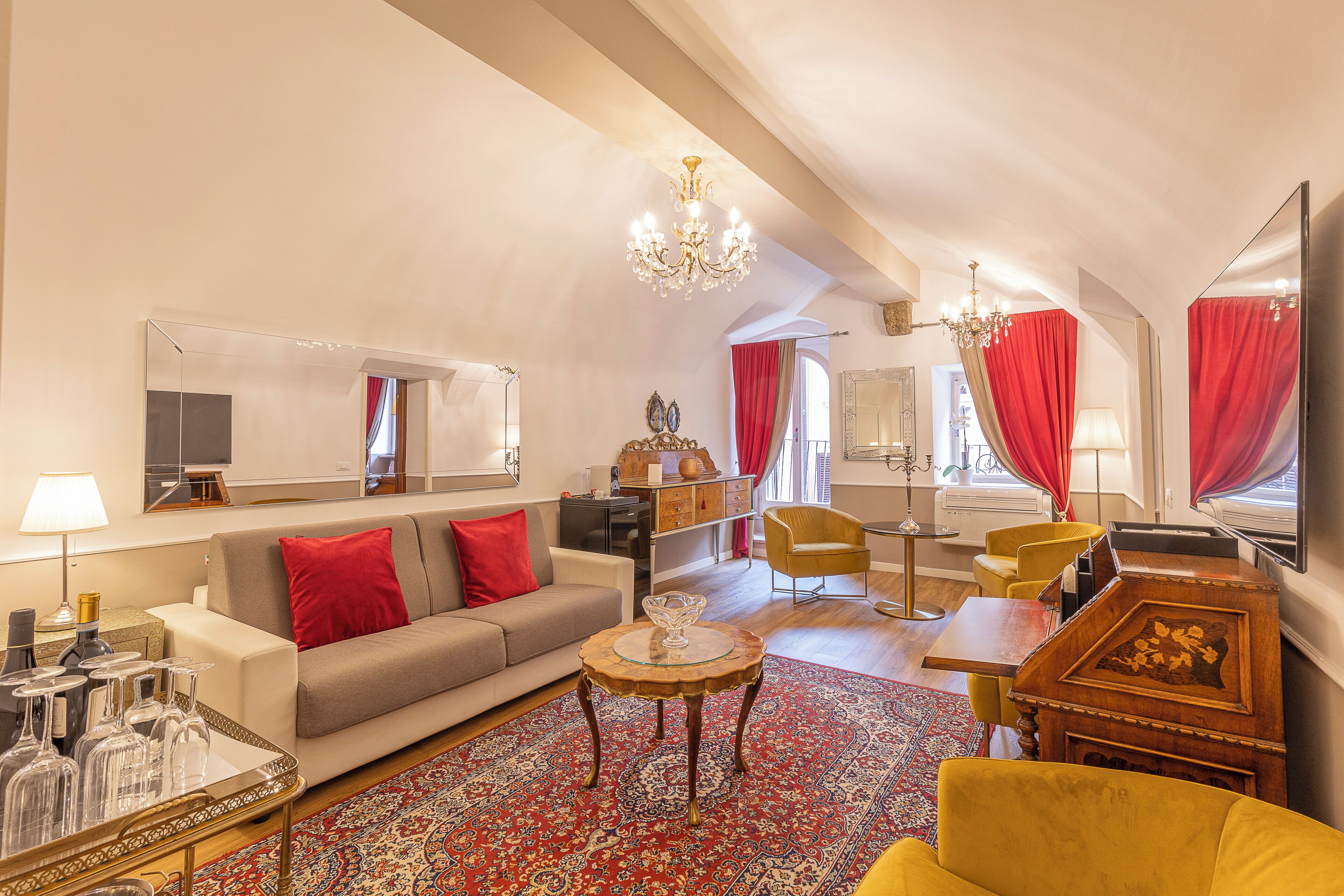 Amplia sala de estar con sofá, sillones, una mesa de centro y una mesa de comedor. Se observa una araña, un espejo grande y una cortina roja.