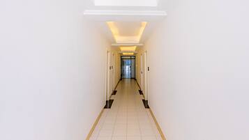 A long, narrow hallway with white walls and a tiled floor, leading to a door at the end.