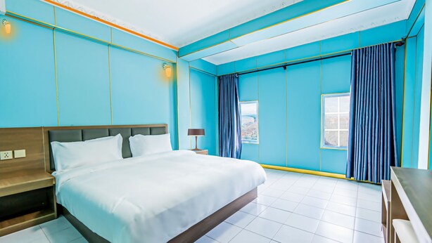 A modern hotel room with a large bed, a bedside table, a nightstand, a window with curtains, and a view of the city. - Chaleunxay Hotel (Vientiane)