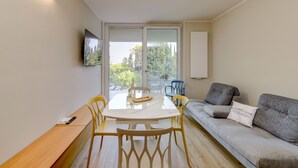 A modern living room with a dining table, chairs, a sofa, and a TV mounted on the wall. - MGH - Lake & Love Apartment (Gardone Riviera)