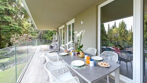 A dining area with a table set for four, surrounded by white chairs, overlooking a garden with trees and a pond. - MGH - Lake & Love Apartment (Gardone Riviera)