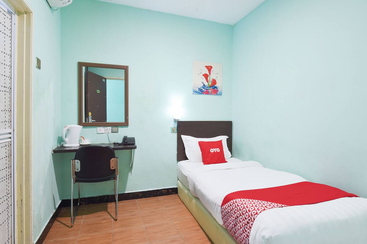 Een hotelkamer met een bed, een bureau met stoel, een spiegel en een schilderij aan de muur.