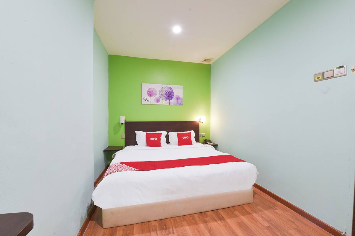 Een netjes opgemaakt bed met witrood beddengoed, een houten vloer en een groene wand met een ingelijst kunstwerk erboven.