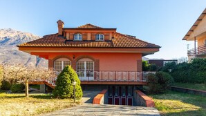 Ein zweistöckiges Haus mit rotem Ziegeldach, einem Balkon mit schmiedeeisernem Geländer und einer Bergkulisse.