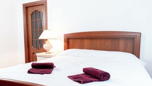 Ein ordentlich bezogenes Bett mit Holz Kopfteil, ein Nachttisch mit Lampe und eine Tür mit Glasfenster.