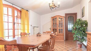 Ein Essbereich mit Holztisch und Stühlen, einer Kristallleuchtre, einer Kübelpflanze und einem Schrank mit Glastüren.
