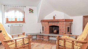 Ein gemütliches Wohnzimmer mit Kamin aus Backsteinen, zwei Holzstühlen, einer Heizung und einem Fenster mit Spitzenvorhängen.