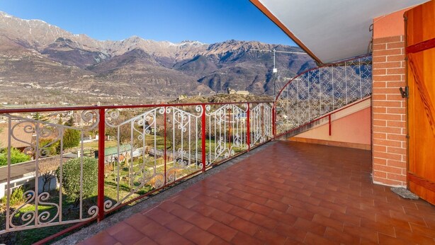 Ein Balkon mit Metallgeländer, der auf eine gebirgige Landschaft blickt.