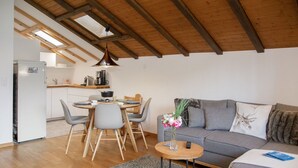 A modern living room with a grey sofa, a dining table with chairs, a small wooden coffee table, and a kitchen area with a white refrigerator. - Lovely apartment for 5 guests with WIFI, pool, TV, balcony and panoramic view (Falera)