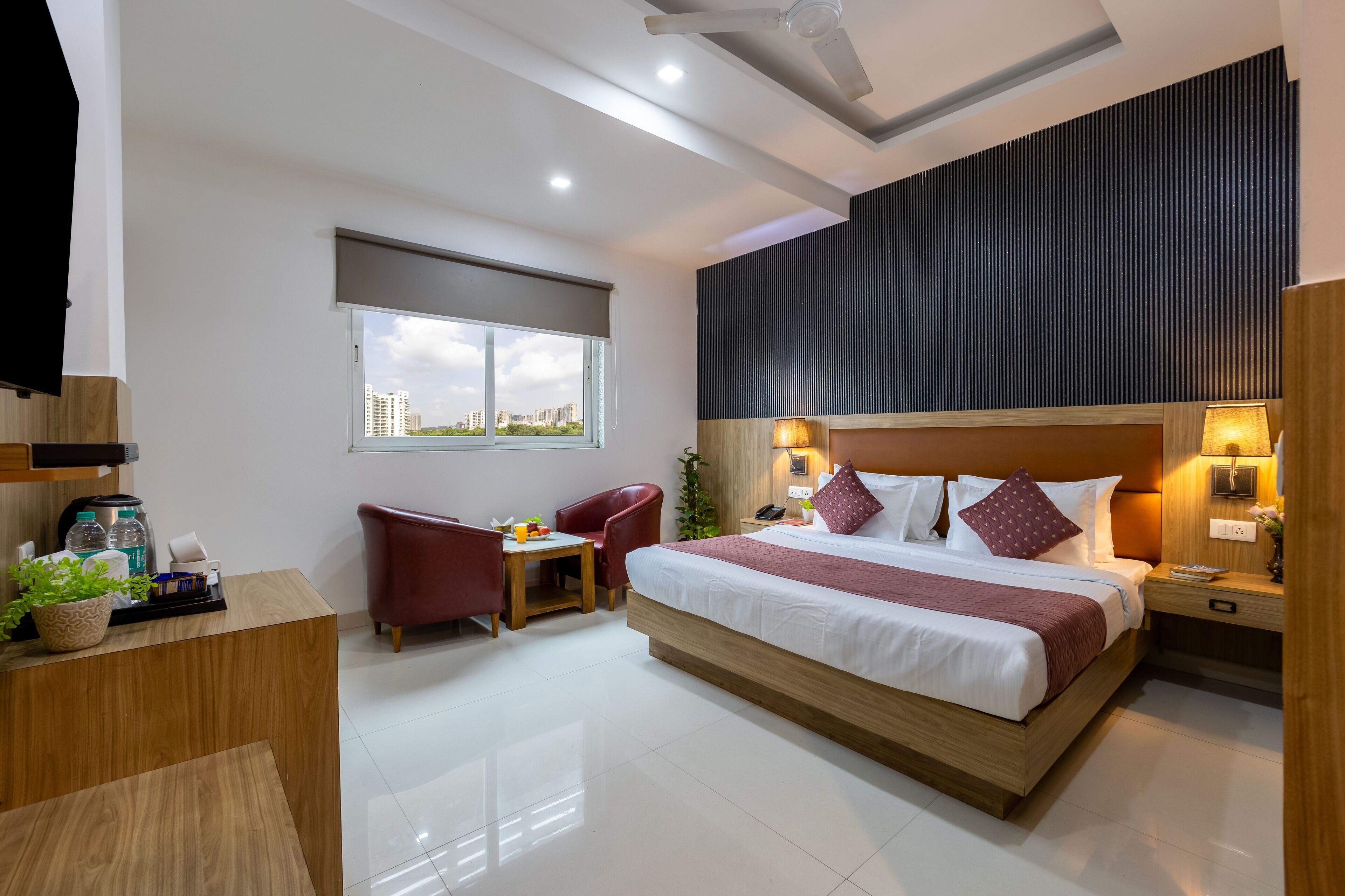 A modern hotel room with a large bed, a desk, a chair, a small table, and a window with a city view.