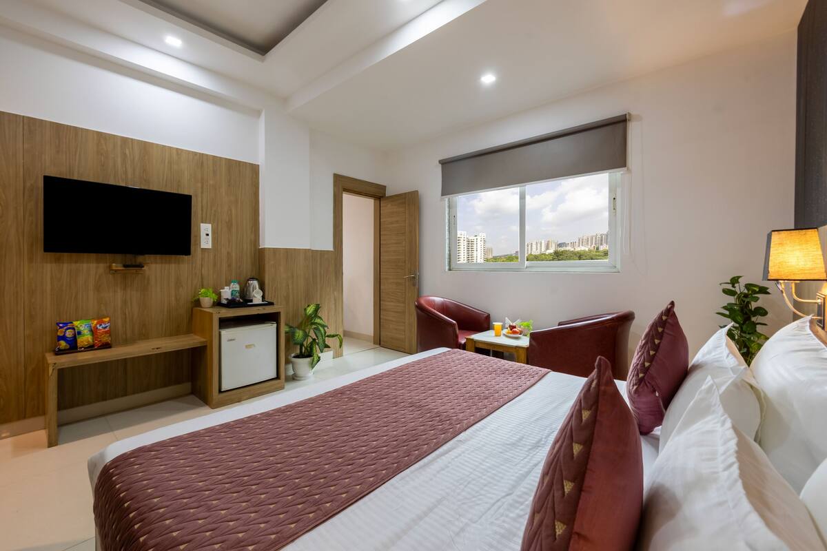 Ein modernes Hotelzimmer mit einem großen Bett, einem Schreibtisch, einem Stuhl, einem Fernseher und einem Fenster mit Blick auf die Stadt.