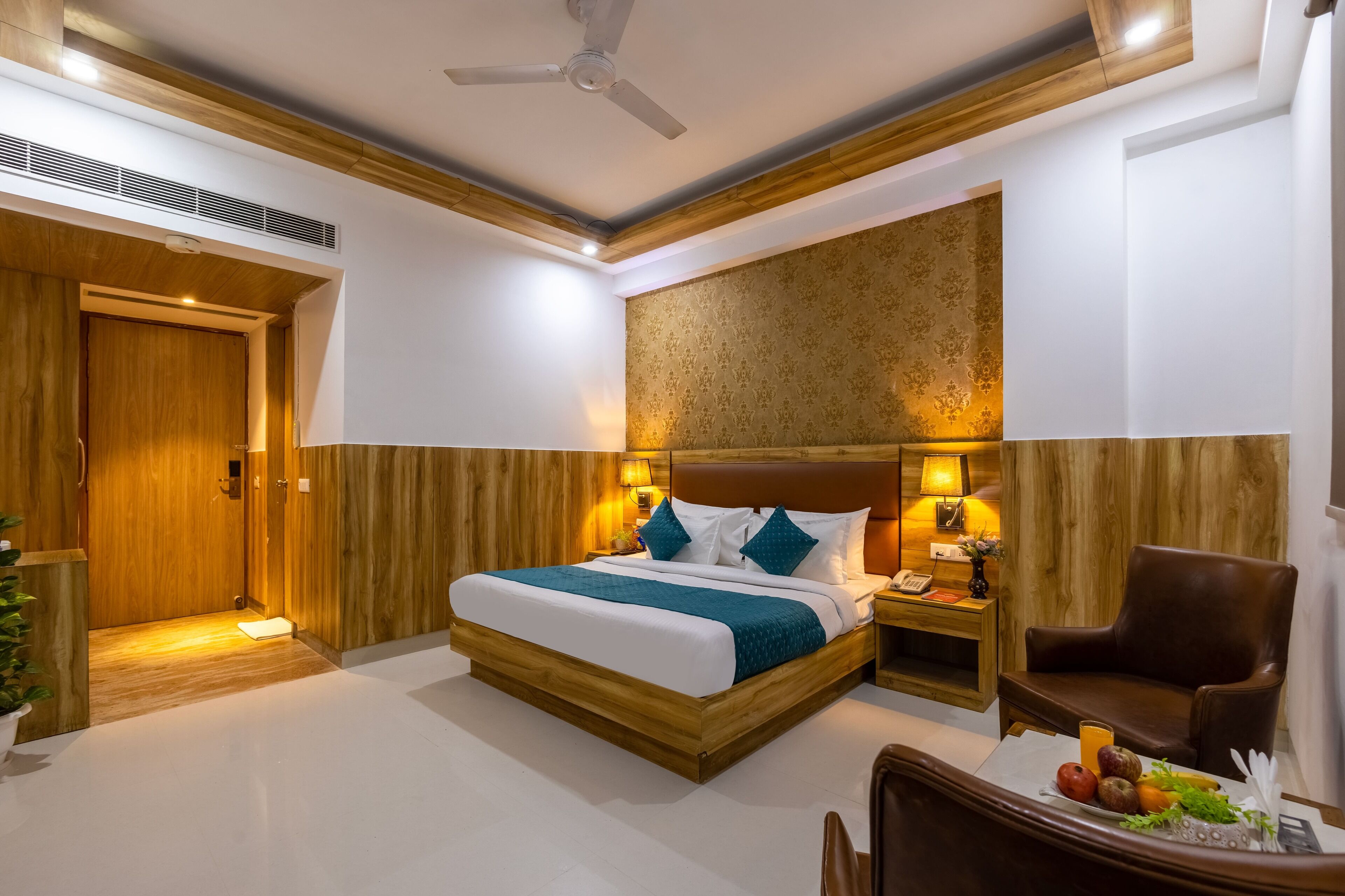 A modern hotel room with a wooden bed, a nightstand, a chair, and a ceiling fan.