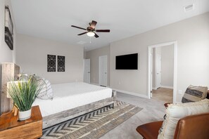 A bedroom with a bed, a ceiling fan, a TV, and a door leading to another room.