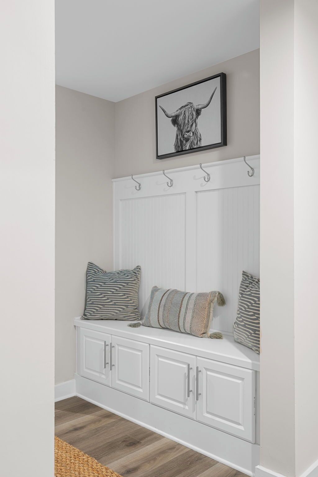 A white bench with a cow head artwork above it, and a white cabinet with drawers below.