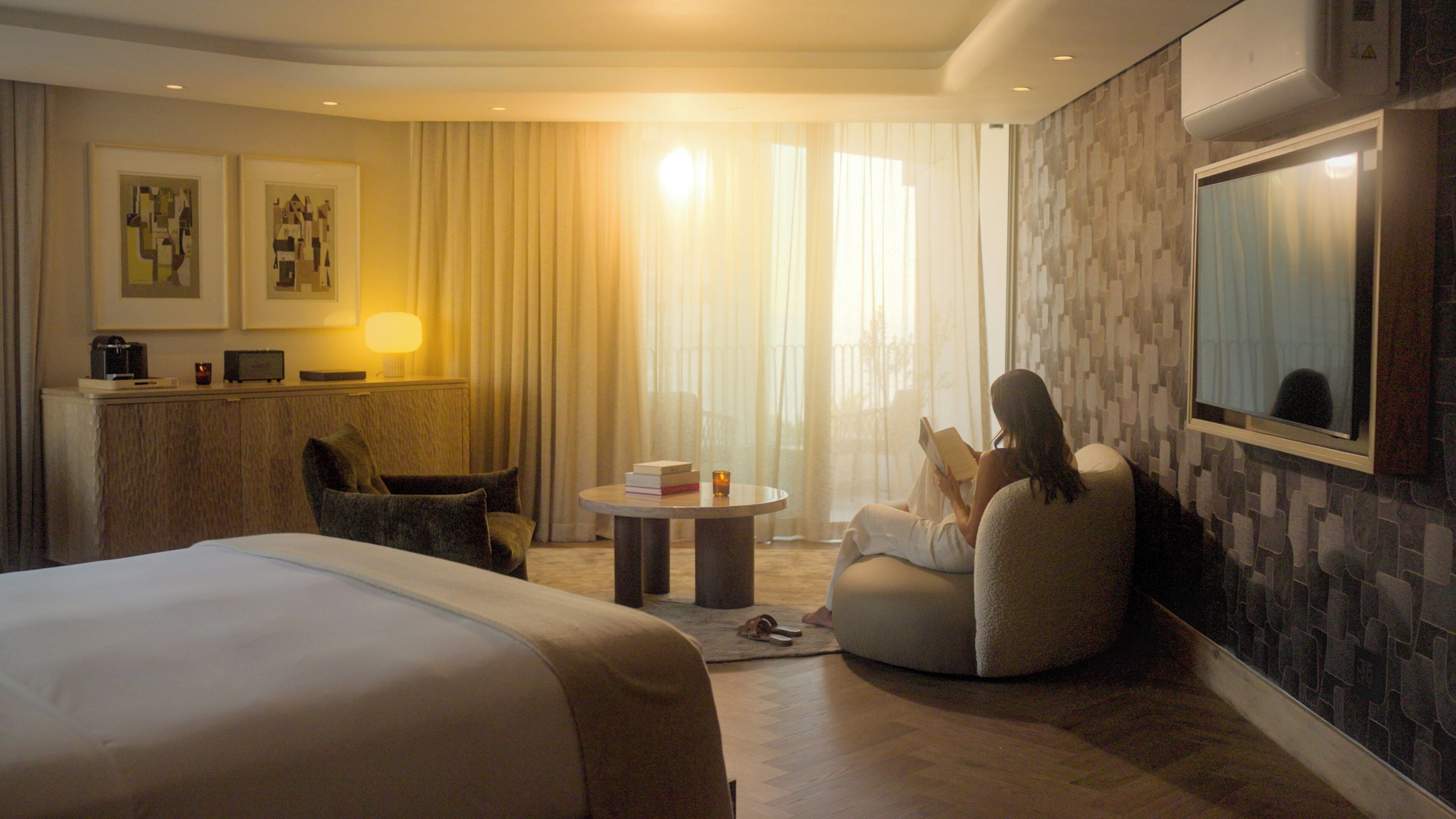 A hotel room with a bed, a round table with books and a candle, a chair, and a large mirror on the wall.