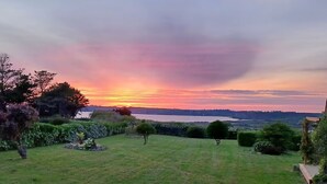 A sunset over a grassy field with trees and a distant view of a body of water.