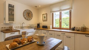A kitchen with a wooden table, a clock, and a window with blinds.