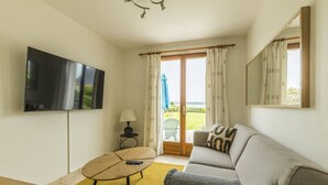A living room with a flat-screen TV, a sofa, a coffee table, and a view of a garden through a sliding glass door.