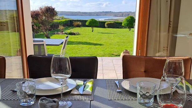 A dining table set for two with a scenic view of a grassy field and a body of water.
