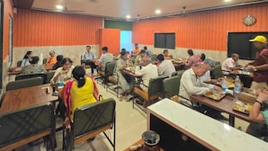 Una cafeteria amb diverses taules i cadires, persones dinant i un rellotge a la paret.