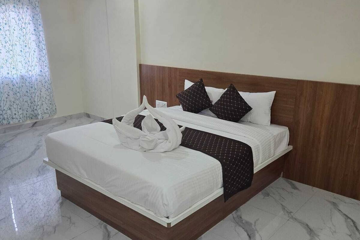 A hotel room with a marble floor, a wooden headboard, and a bed with white bedding and black pillows.