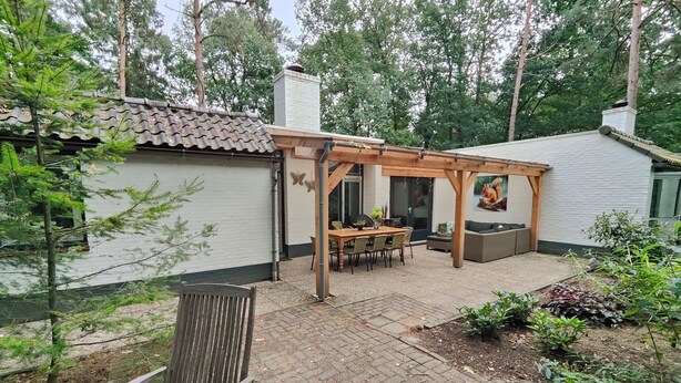 Un patio con mesa y sillas de madera, un banco de madera y una zona ajardinada con plantas.