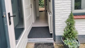 Una entrada de casa con una puerta, una planta pequeña en maceta y un cartel con un número en la pared.