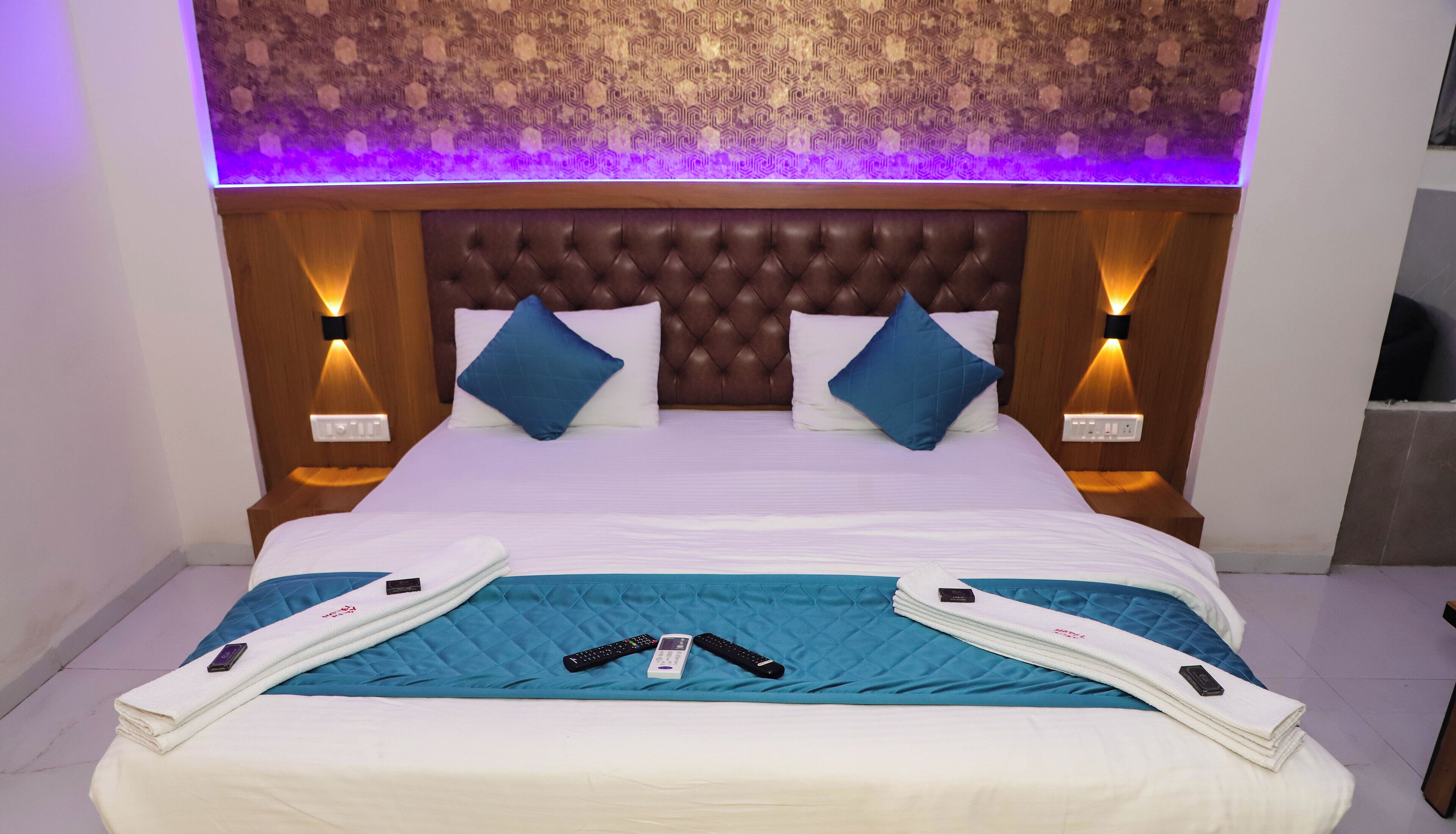 A hotel room with a tufted headboard, two bedside lamps, a bed with white linens, and a blue quilt.