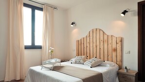 A bedroom with a wooden headboard, a bed with white bedding, a bedside table with a lamp, and a window with curtains. - Tenute Delogu (Sassari)