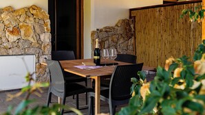 A dining area with a stone wall, a wooden table, and black chairs. - Tenute Delogu (Sassari)