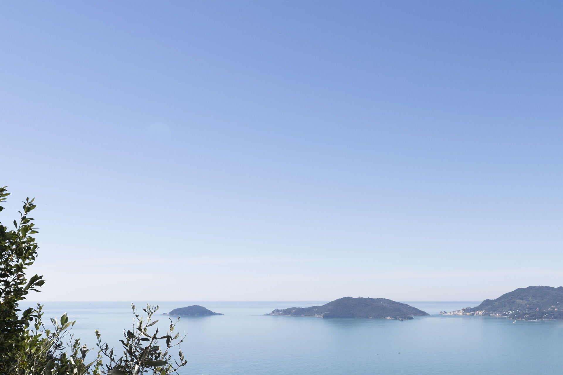 Un paisaje costero con cielos despejados, mar tranquilo y islas a lo lejos.