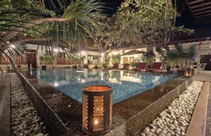 A nighttime pool area with a clear pool, surrounding plants, and a candle.
