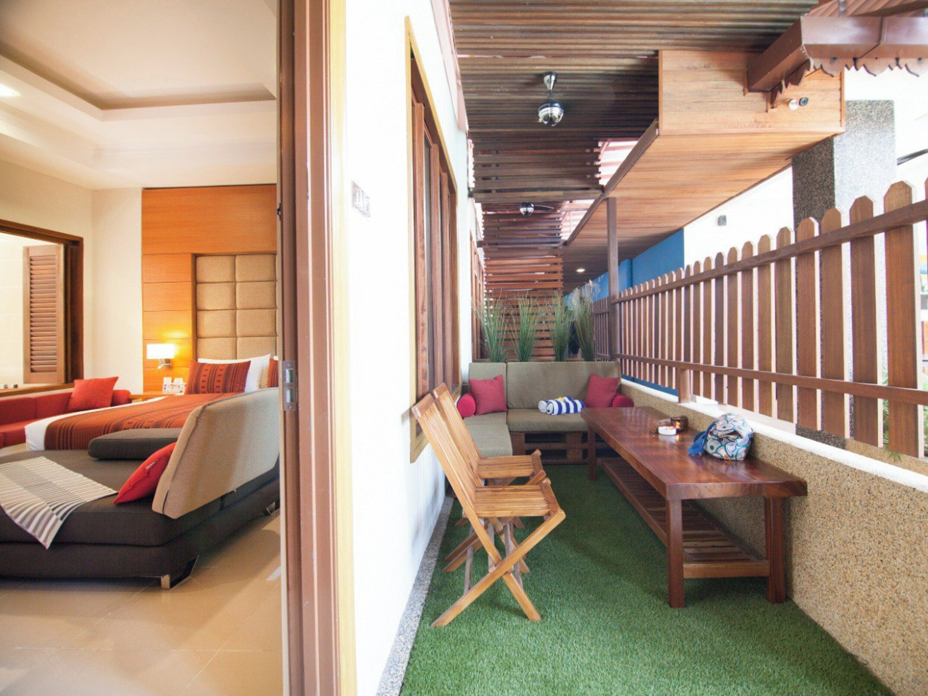 A hotel room with a bed, a sofa, a wooden table, and a green artificial turf floor.