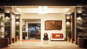 L'entrée d'un hôtel, avec un canapé rouge, des plantes en pot et une enseigne indiquant « TELAGA TERRACE LANGKAWI ».
