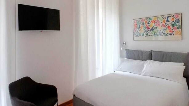 A bedroom with a bed, a chair, a flat-screen TV, and a painting on the wall.