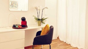 A modern, minimalistic room with a wooden floor, a white desk, a black chair with a yellow cushion, a small potted plant, and a wall-mounted mirror.