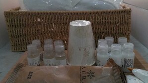 A set of toiletries including bottles and a container, arranged on a tray in a room with a wicker basket in the background.