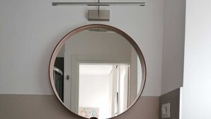 A bathroom with a round mirror, a white sink, and a wooden countertop.