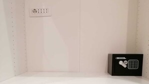 A white desk with a black electronic device on it, a power outlet, and a white drawer below.