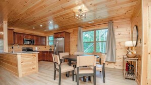 Interior de una cabaña de madera con cocina, comedor y un amplio ventanal.